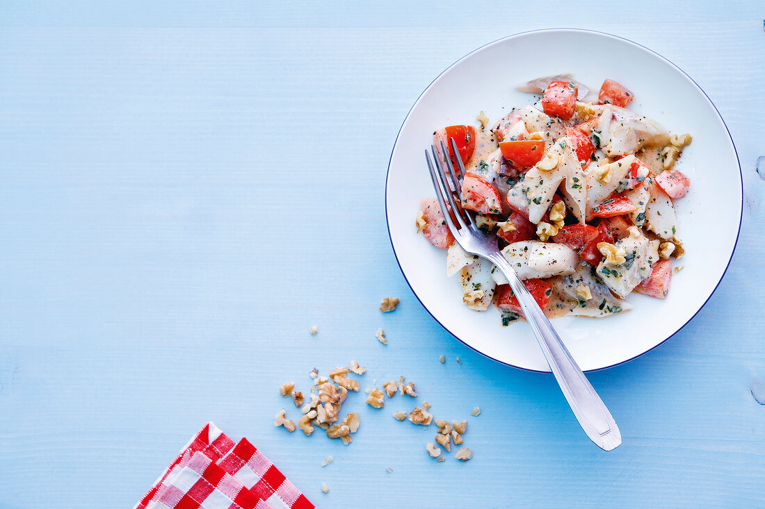 Salad with fish, tomatoes, herbs and walnuts on plate
