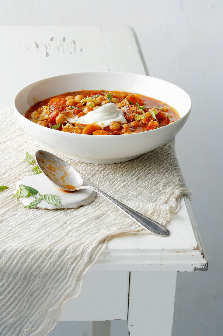 Bowl of chick pea and tomato soup with spoon on table