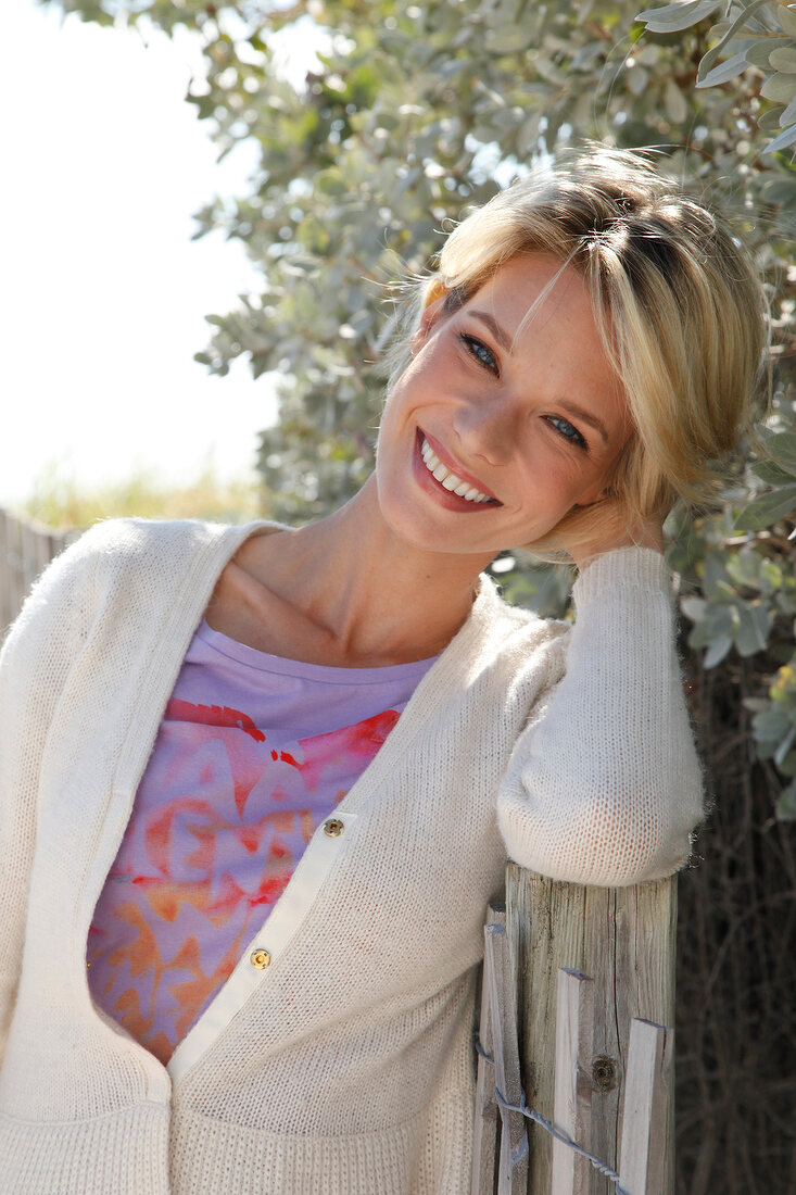 Portrait of pretty blonde woman with short hair wearing top and white cardigan, smiling