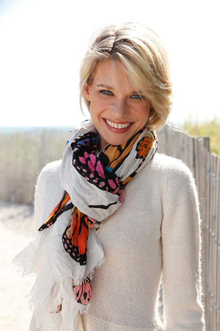 Portrait of beautiful blonde woman wearing white sweater and colourful scarf, smiling