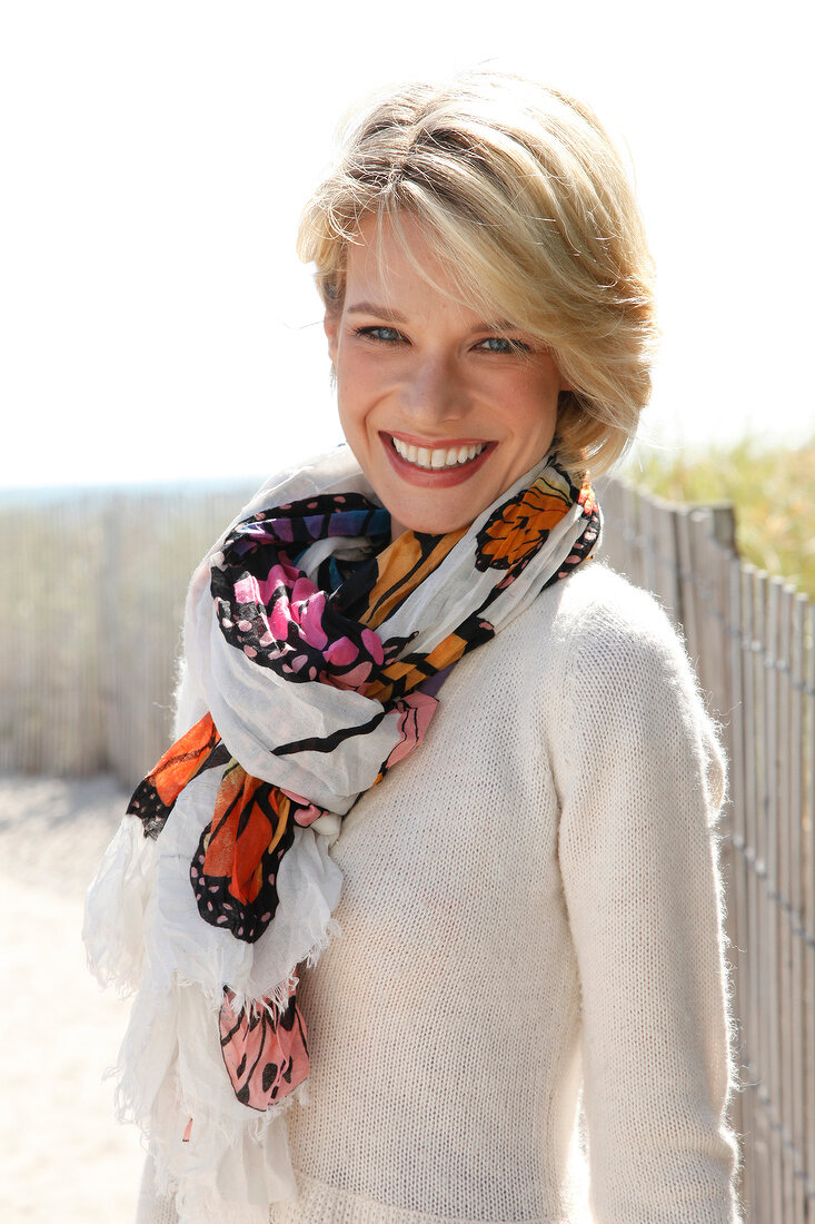 Portrait of beautiful blonde woman wearing white sweater and colourful scarf, smiling