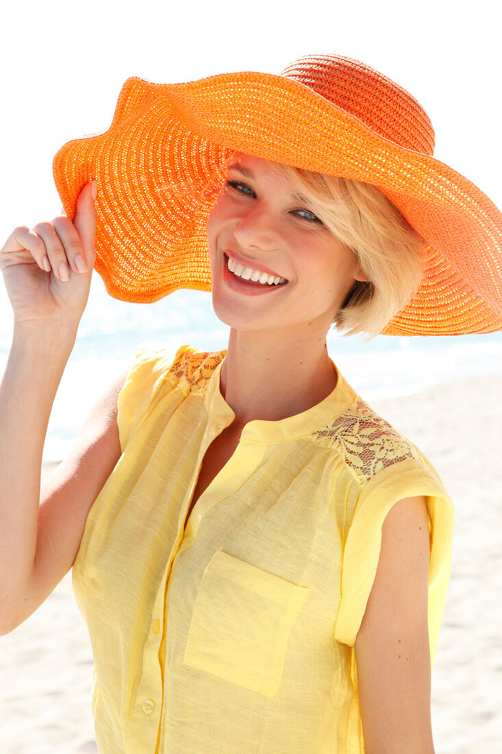 Portrait of happy woman in yellow sleeveless blouse and sun hat enjoying on beach, smiling