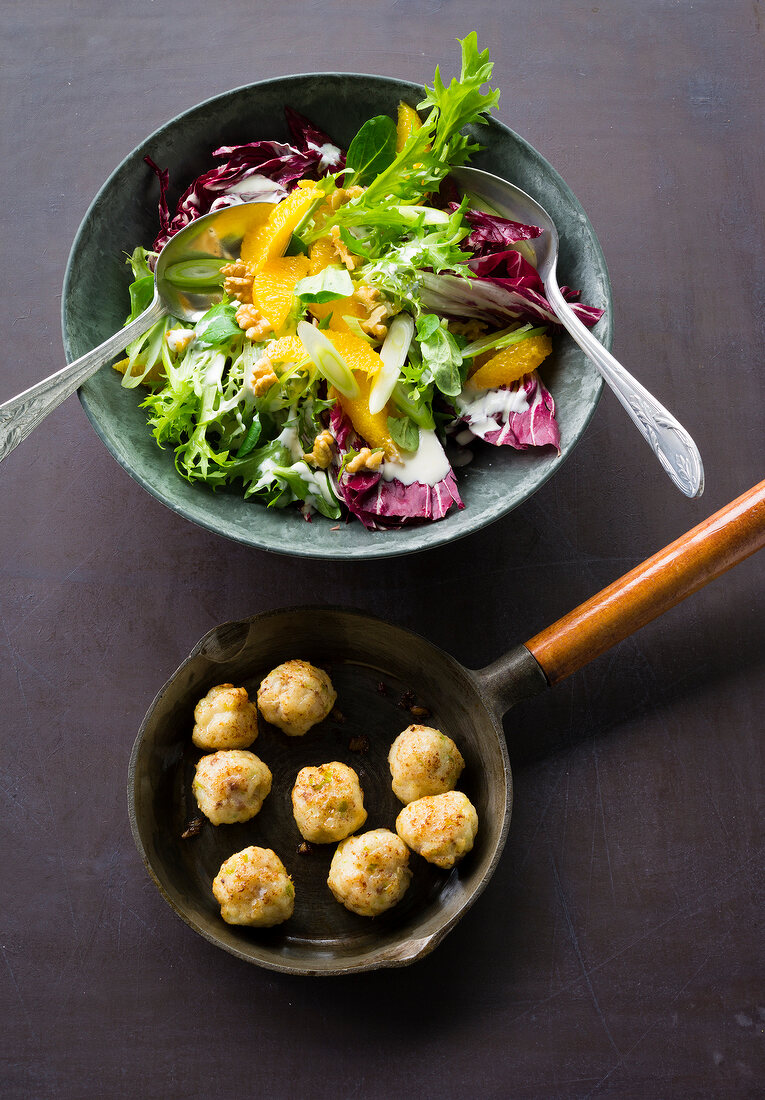 Winter salad with oranges in bowl and fish balls in pan