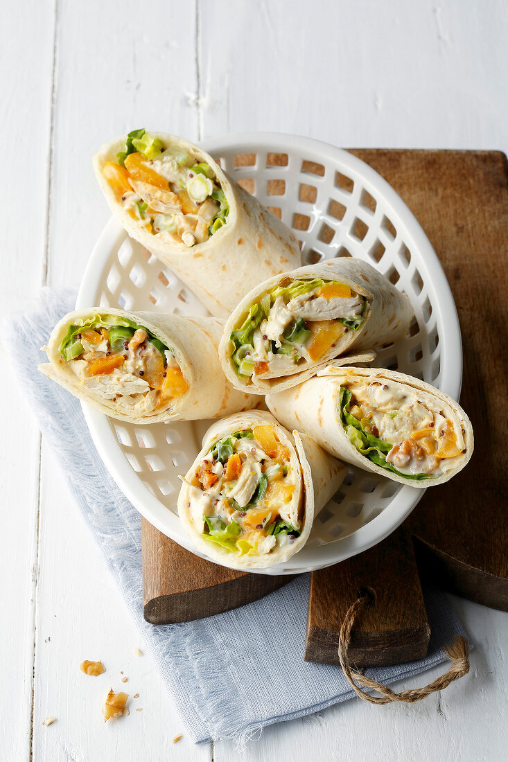 Chicken wraps in basket on wooden board, overhead view