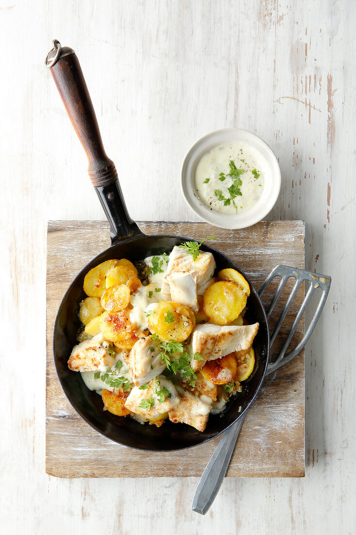 Pannfisch with mustard sauce in frying pan on cutting board, overhead view
