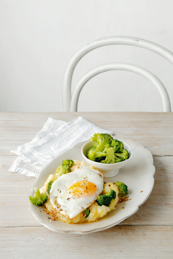 Lemon puree with fried egg on dish and bowl of broccoli on wooden table
