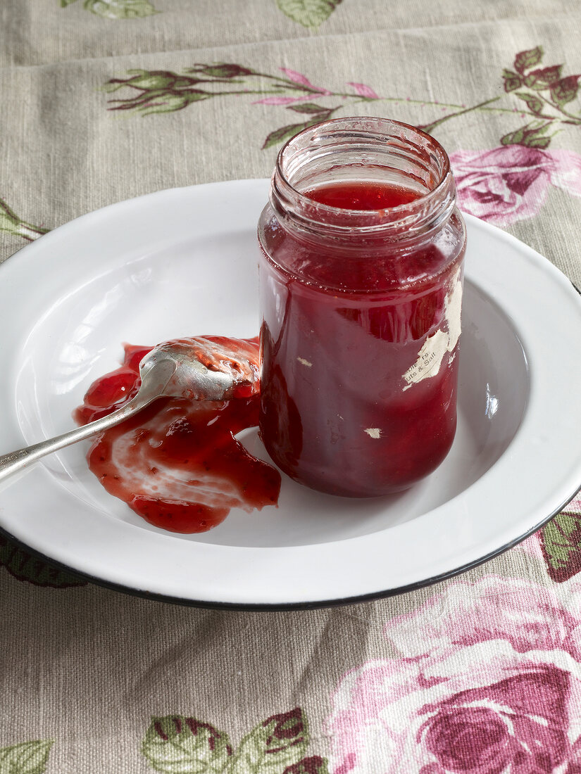 Bottle of rhubarb jelly with strawberries and spoon on plate
