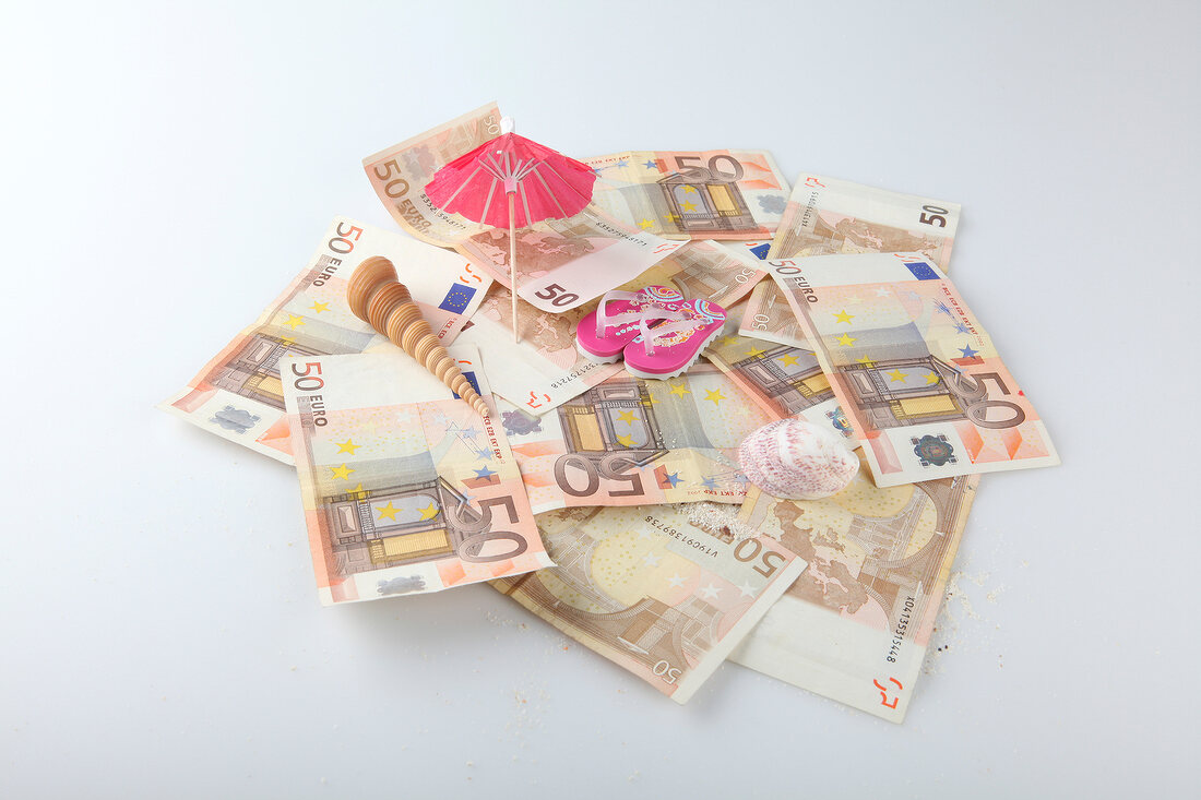 Heap of bills, umbrella, flip-flops and shells on white background