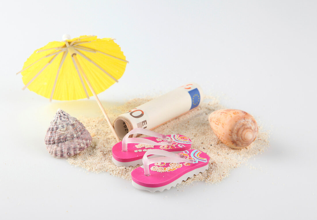 Rolled bills, shell, flip-flops, umbrella on sand on white background