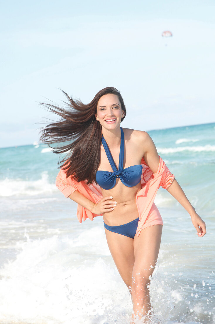 Portrait of beautiful woman wearing blue bikini and blouse standing on beach, smiling