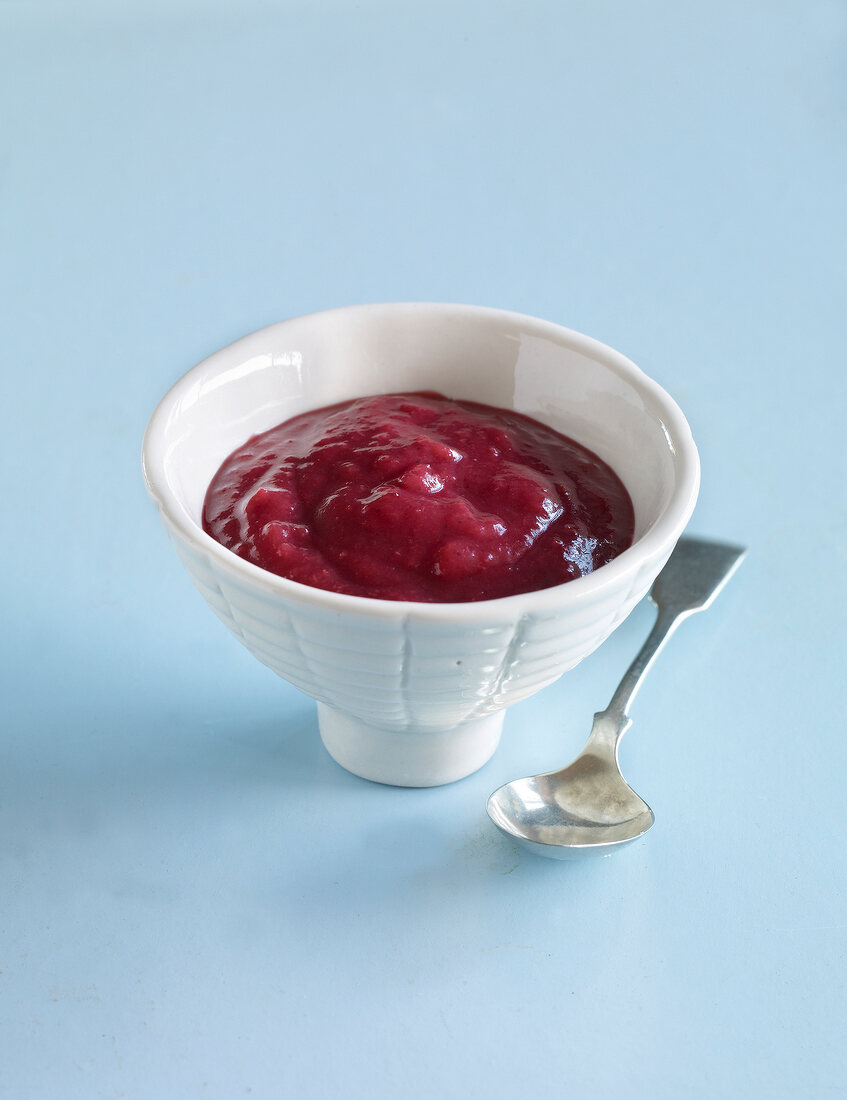 Berries jam in bowl with spoon on blue background