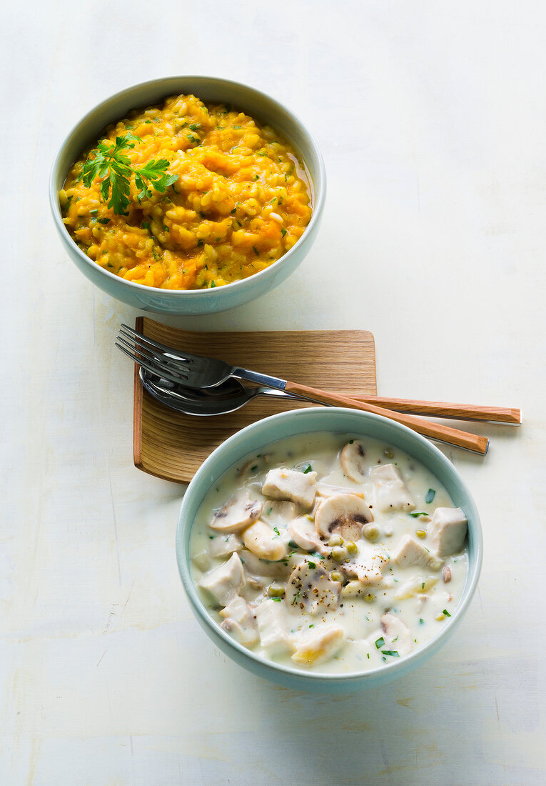 Bowl of pumpkin risotto and chicken fricassee with spoon and fork on white background