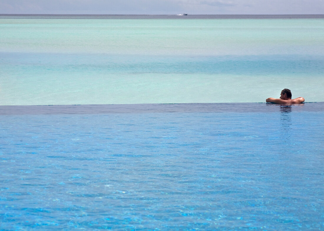 Lonely man relaxing in pool with sea in background in Dhigufinolhu Island, Maldives