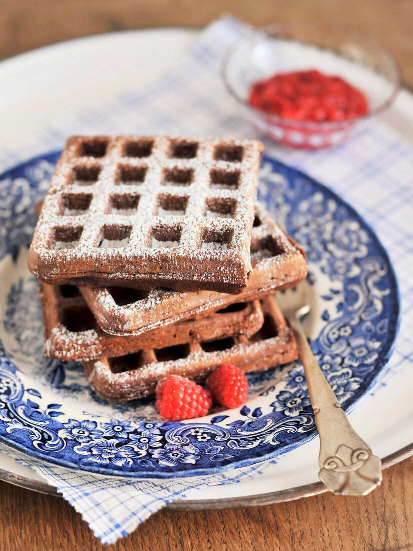Close-up of chocolate wafers with raspberries and icing sugar on plate