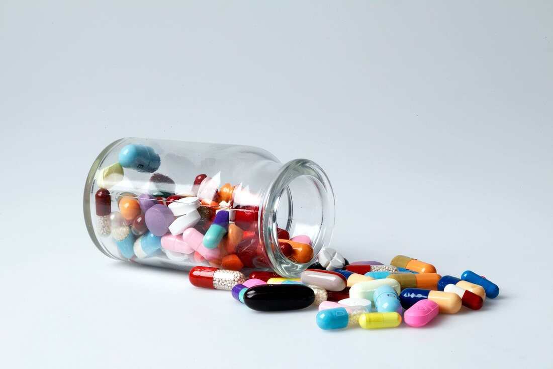 Close-up of glass jar with colourful tablets spilled on white background