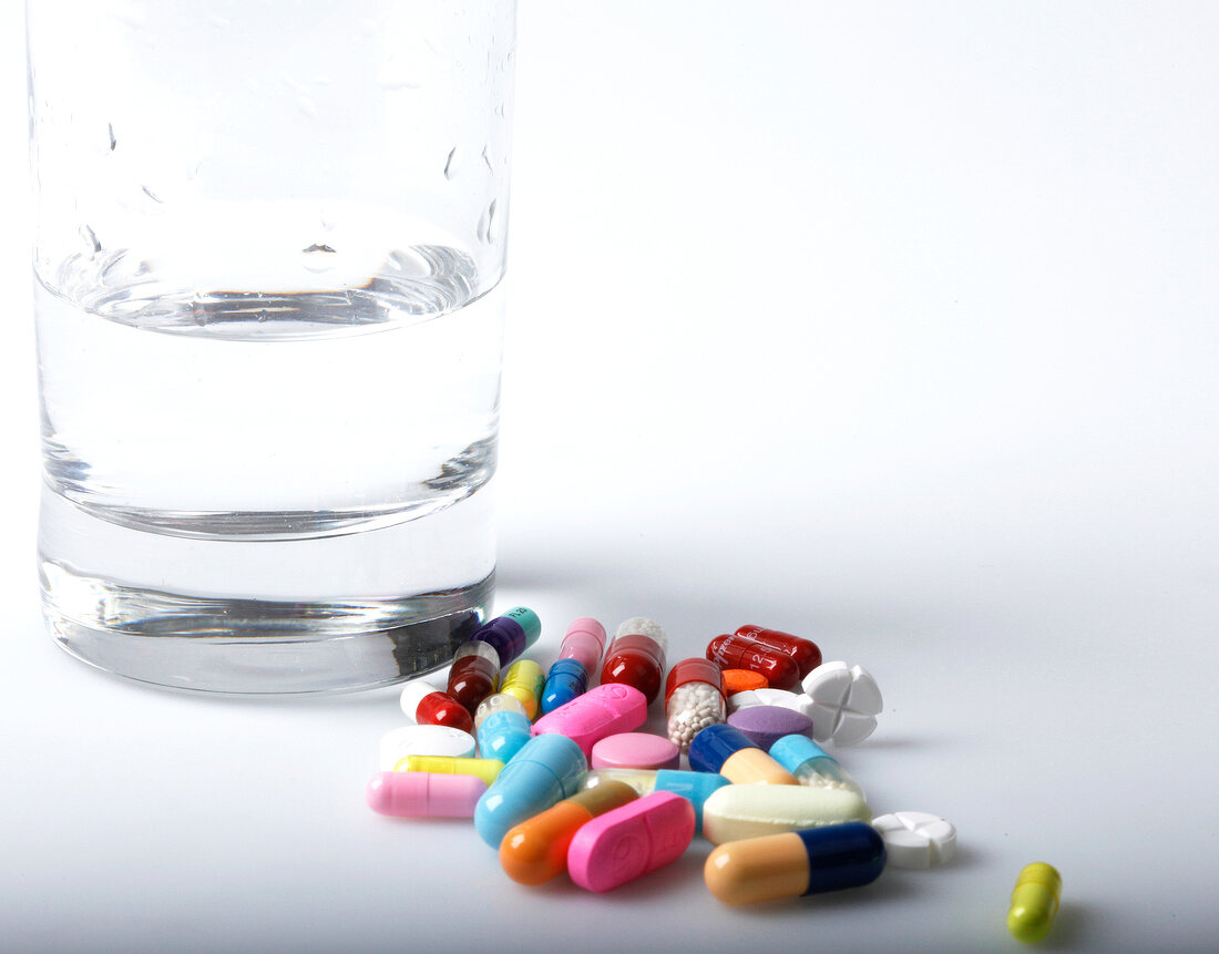Various coloured tablets next to glass of water on white background