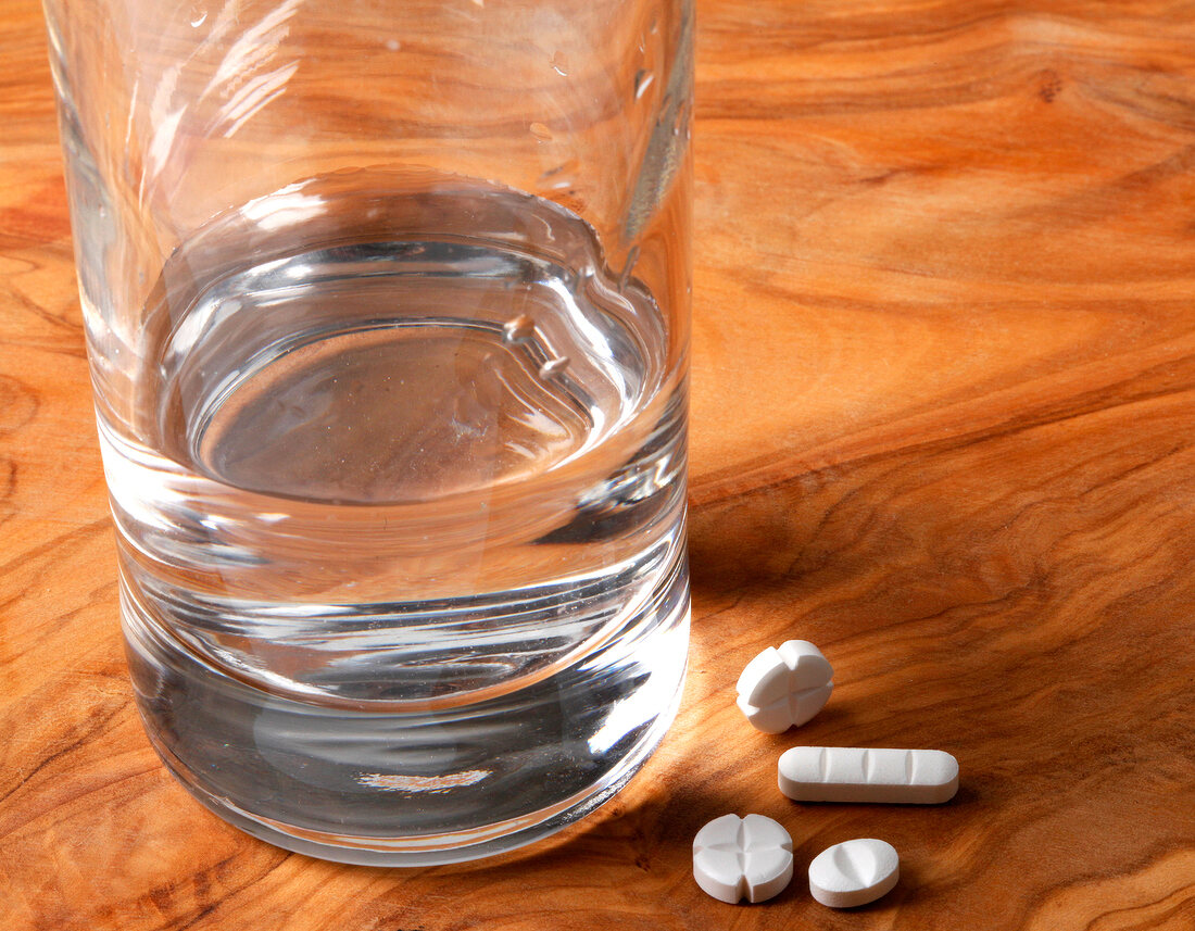 Close-up of tablets and glass of water on wooden table