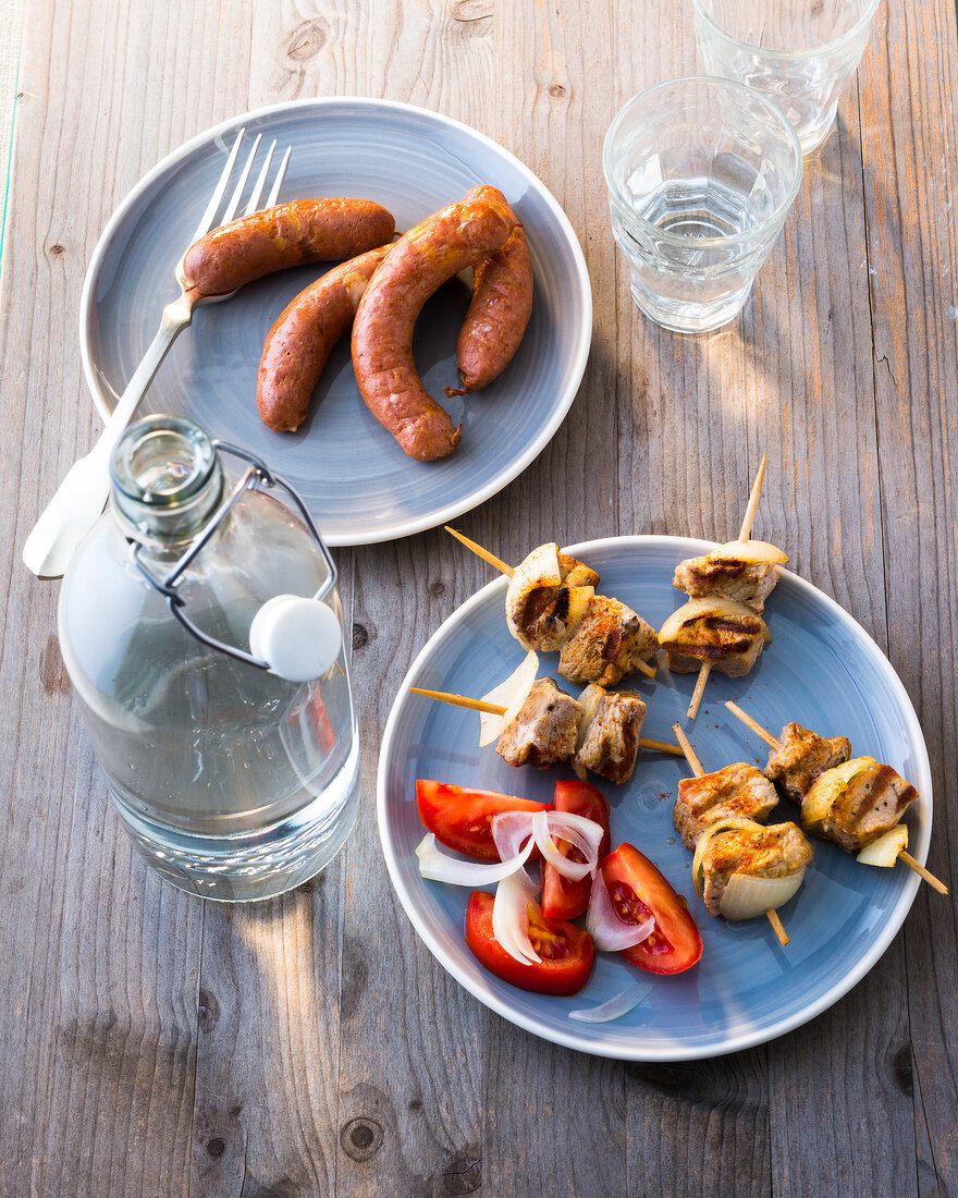 Hot dogs and meat skewers with tomato slices on plate