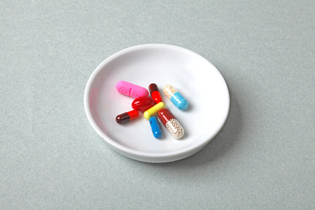 Close-up of small bowl with different colourful tablets on gray background