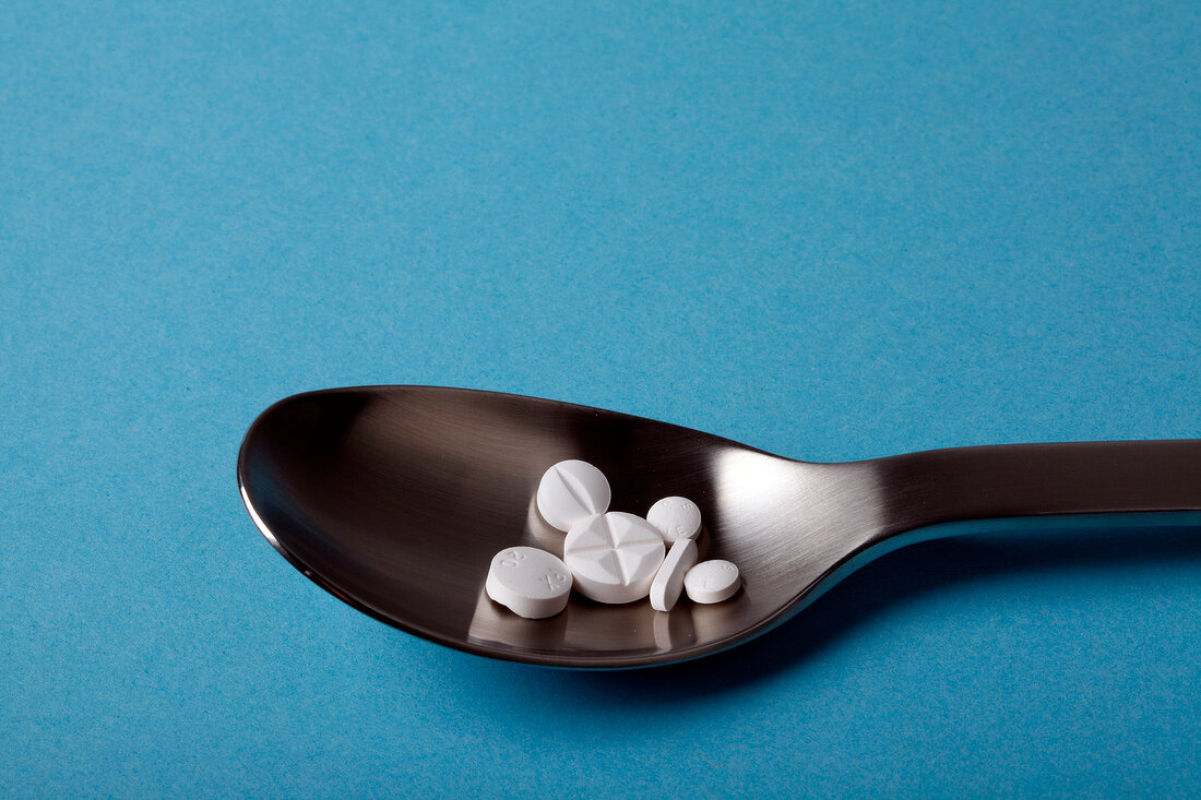 Close-up of spoon with tablets on blue background