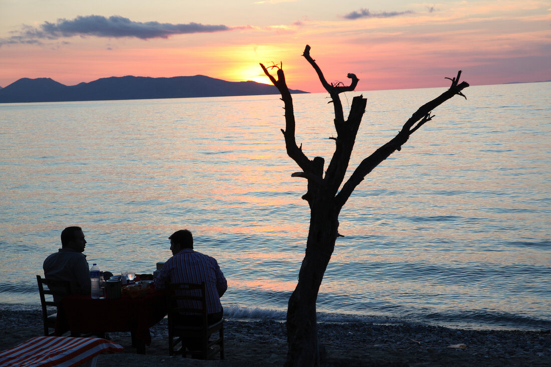Two people sitting by the Mediterranean sea at sunset in Guzelcamli, Aegean, Turkey