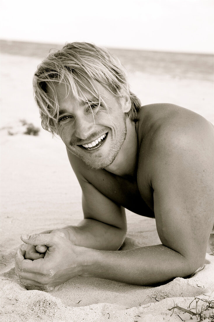 Portrait of happy blonde man having fun while lying on beach, laughing, black and white