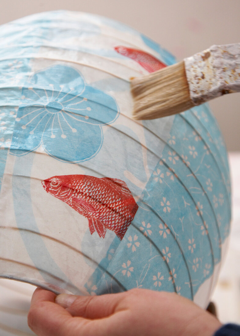 Close-up of person painting colourful lantern with flower and fish motif
