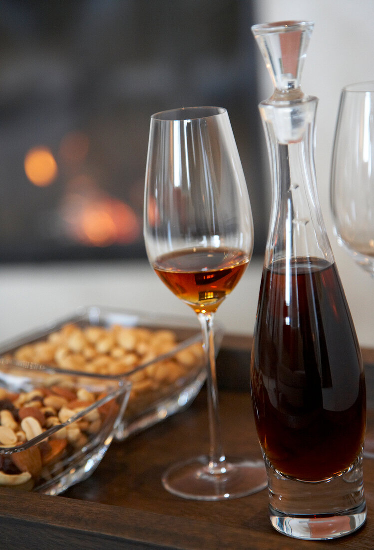 Close-up of liqueur in carafe and glass with bowl of snacks