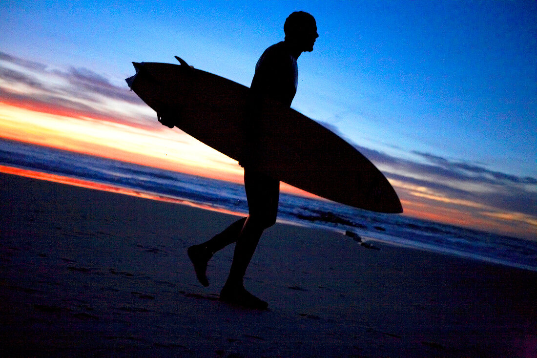 Surfer walking with surfboard on beach at sunset