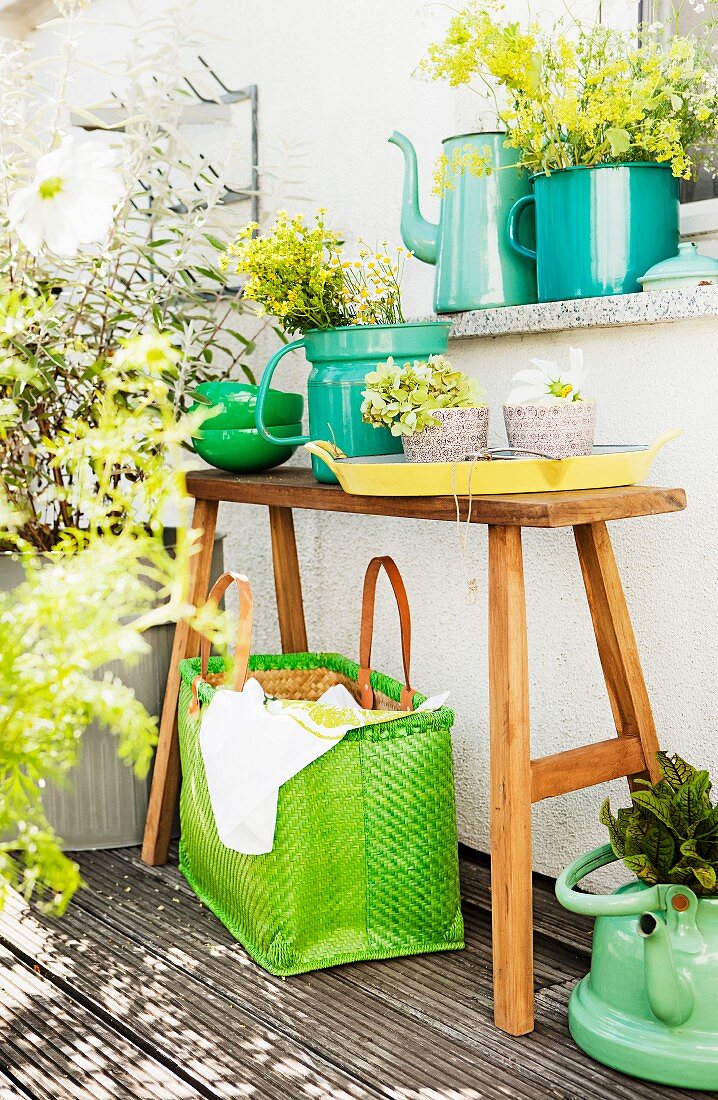 Teakholzbank, Kräuter in Emaillegefäßen und Basttasche auf dem Balkon