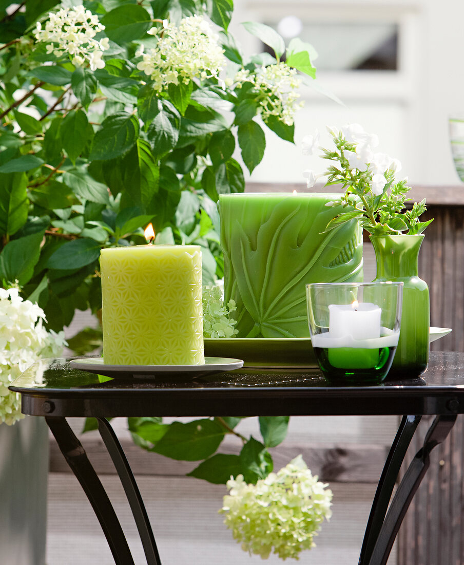 Decorative green lit candles on table with plants around