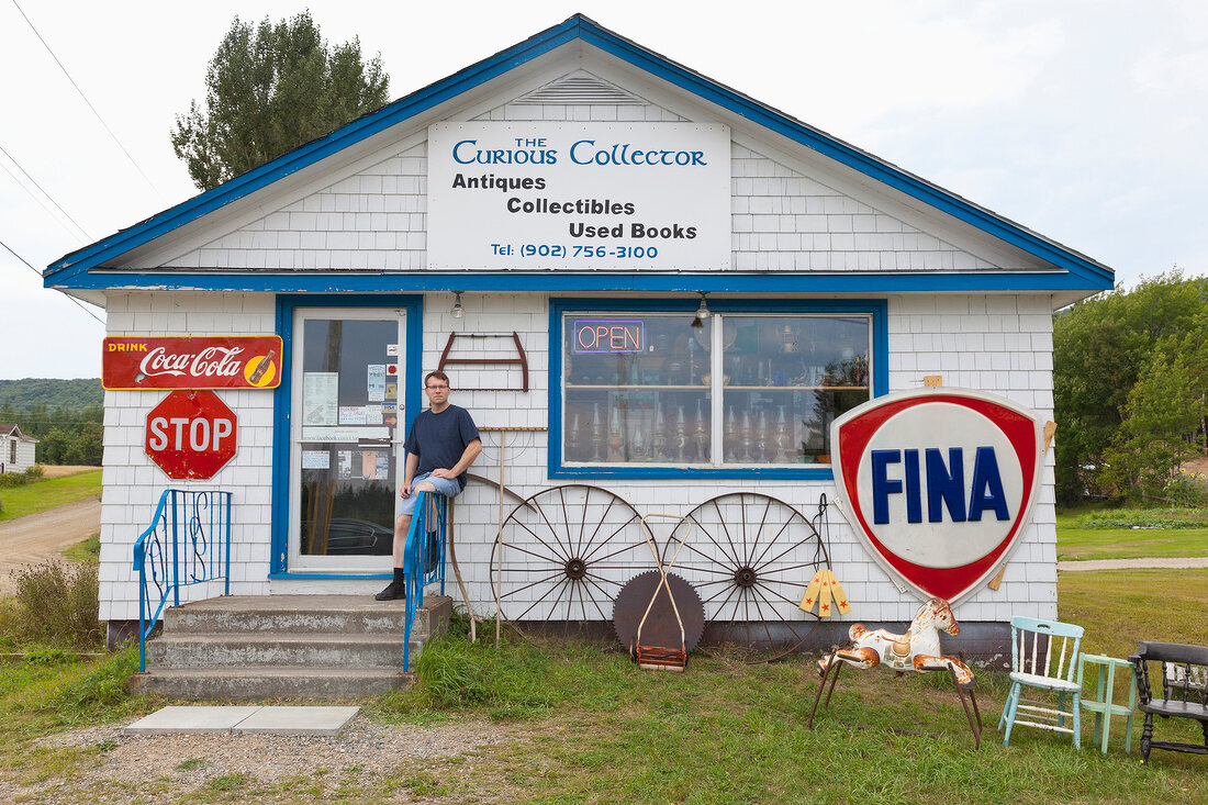 Man sitting outside The Curious Collector shop, Cape Breton Island, Canada