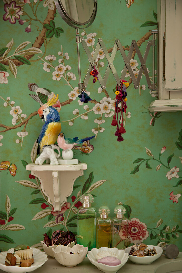 Wallpaper with floral motif, parrot, ceramic, console and vanity mirror against green wall