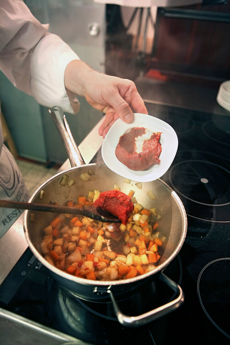 Beef being braised in red wine with stir fried vegetables in pan