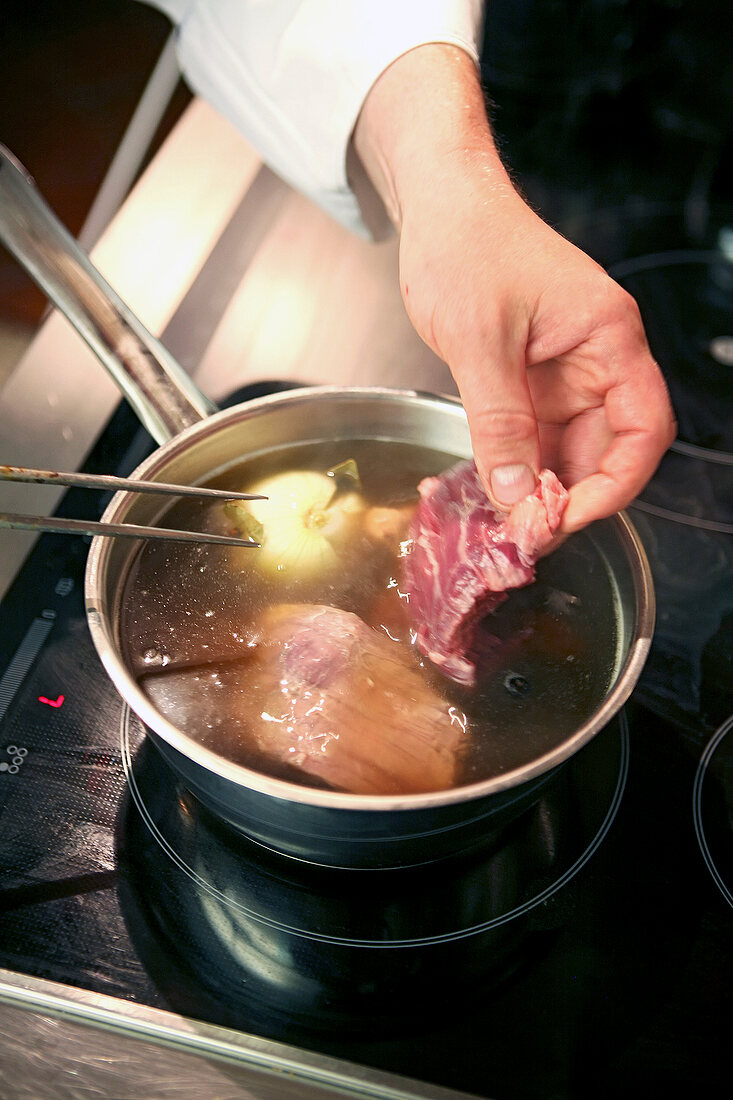 Close-up of man's hand putting onglet, beef, root and meat in broth