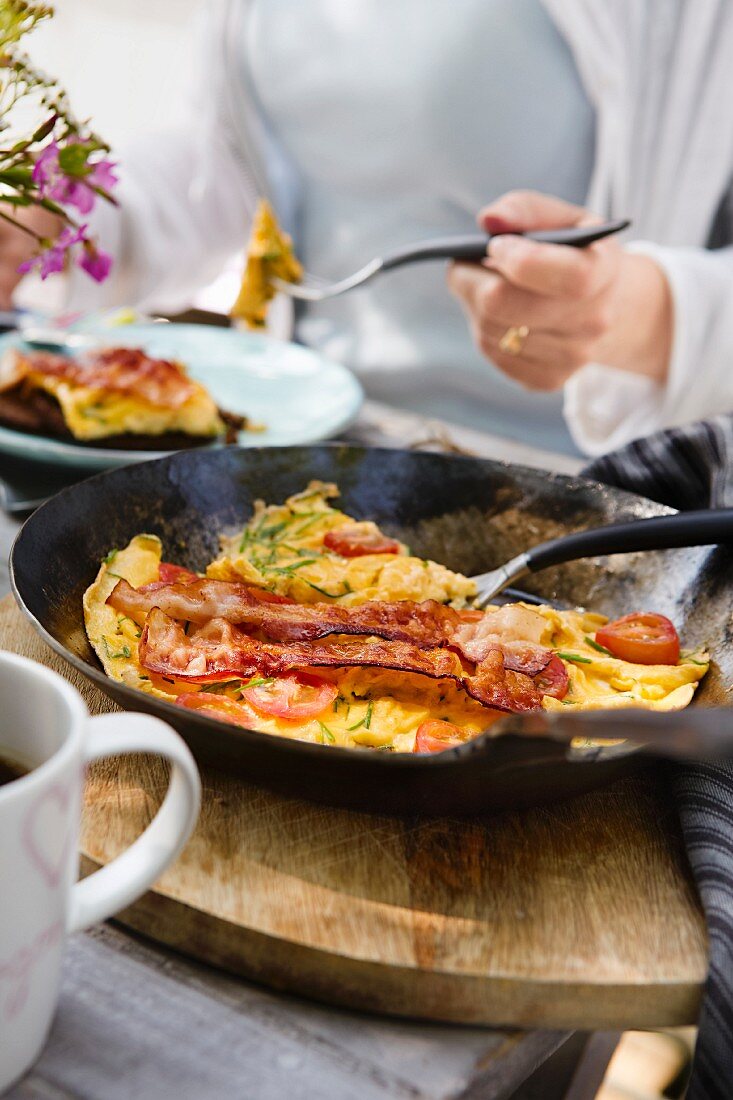 Omelette with bacon and tomatoes in a pan on a table