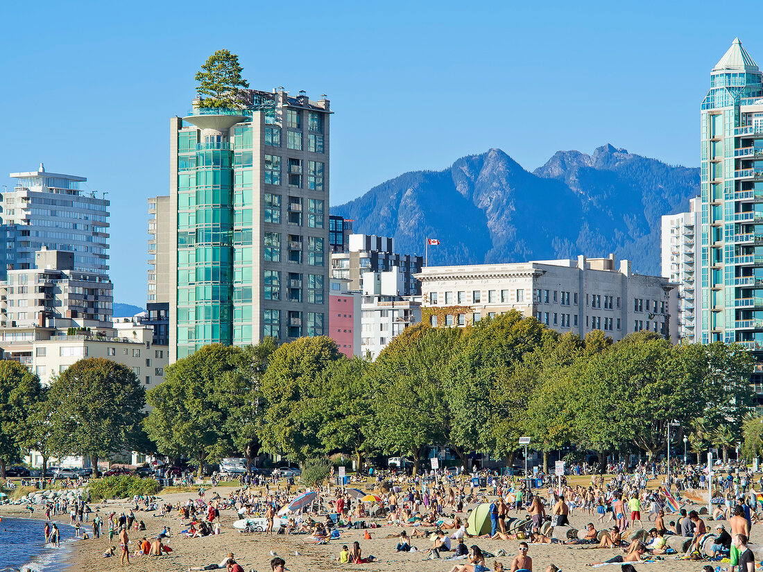 Mountains, hotels and crowded English Bay Beach, Vancouver, British Columbia, Canada