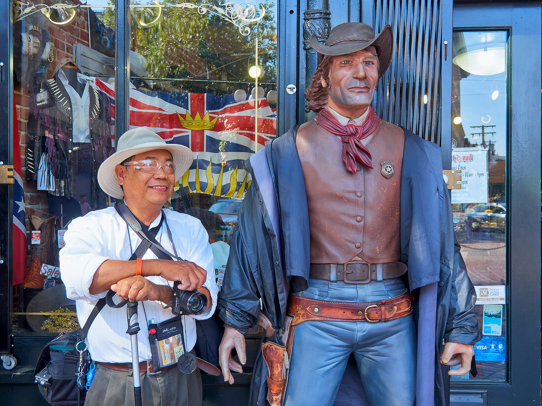 Tourist standing by the cowboy figure in Gastown, Vancouver, British Columbia, Canada