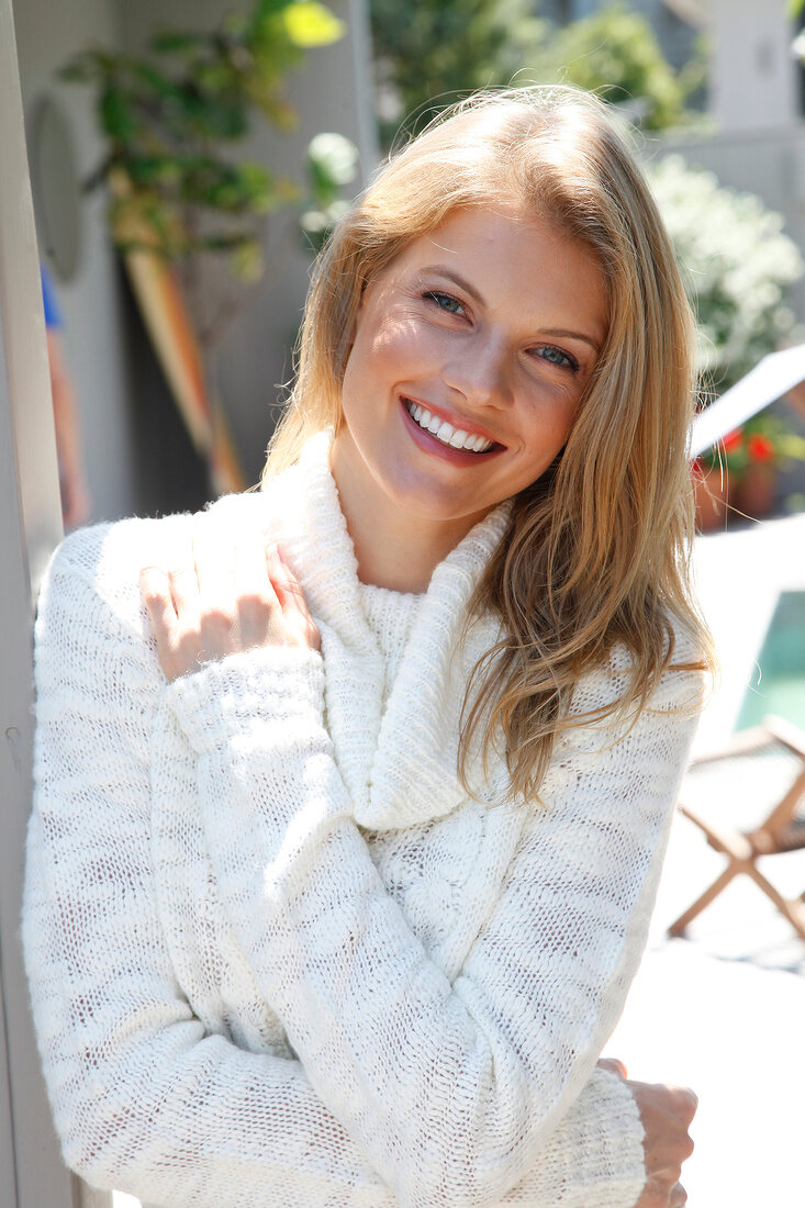 Portrait of blonde woman wearing white turtleneck sweater standing on beach, smiling
