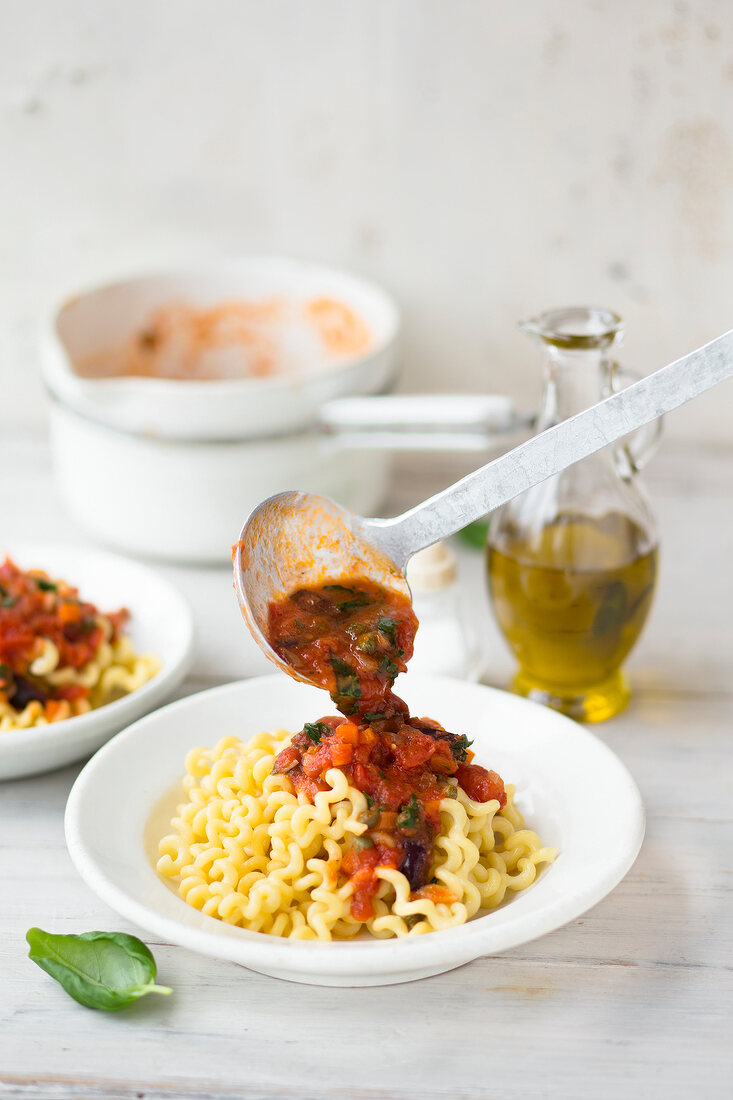 Pouring tomato sauce on pasta spirals in serving dish