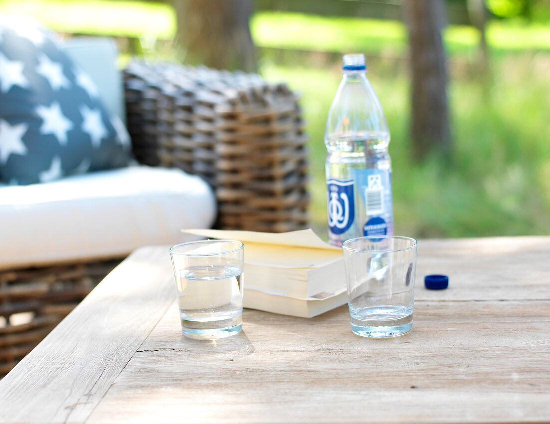 Glasses, bottle and books on wooden table in garden
