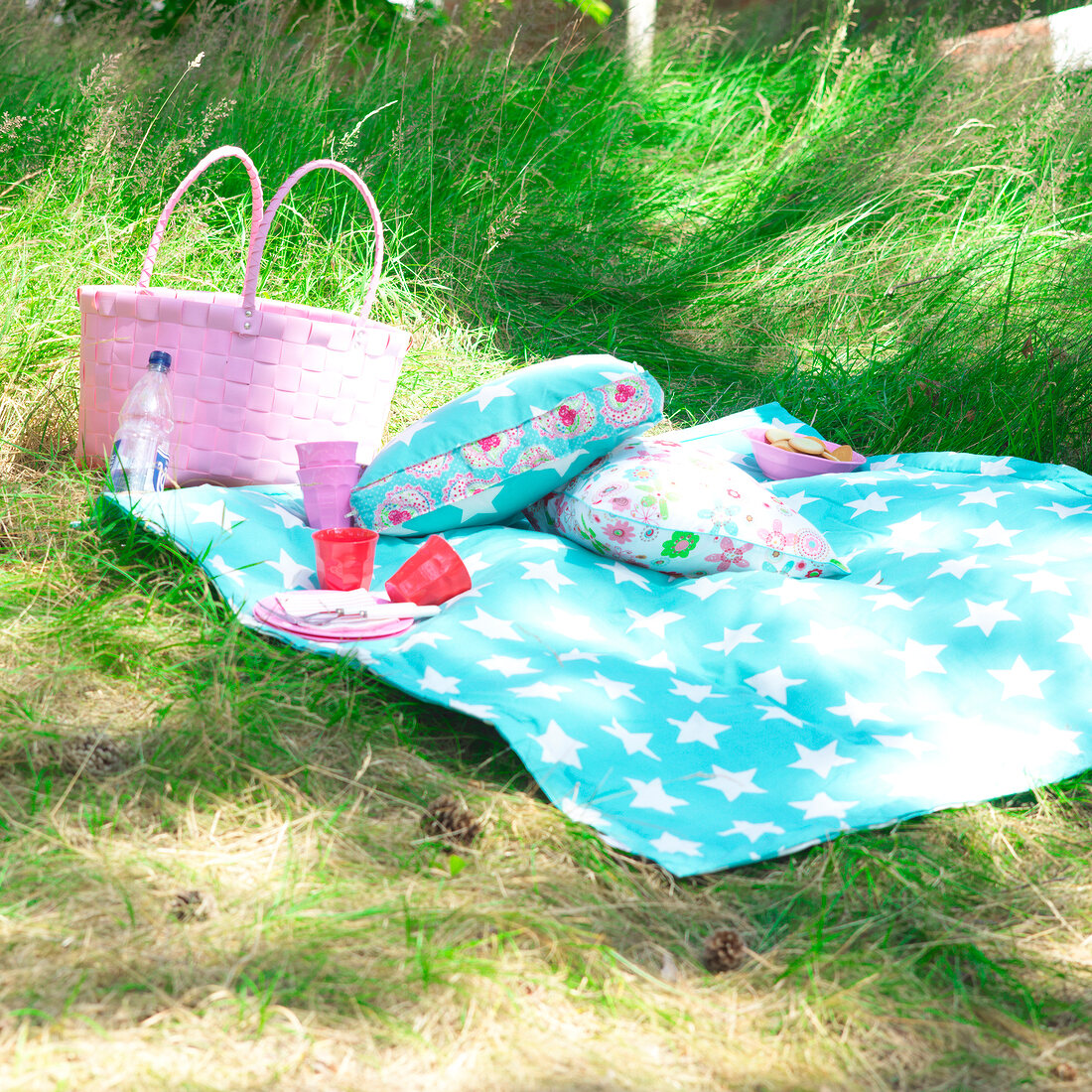 Colourful cushions and blanket with pink wicker basket in garden