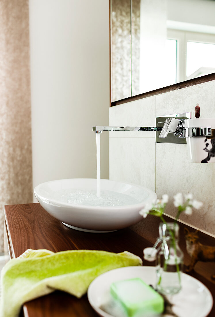 Close-up of faucet with running water, oval sink and green accessories