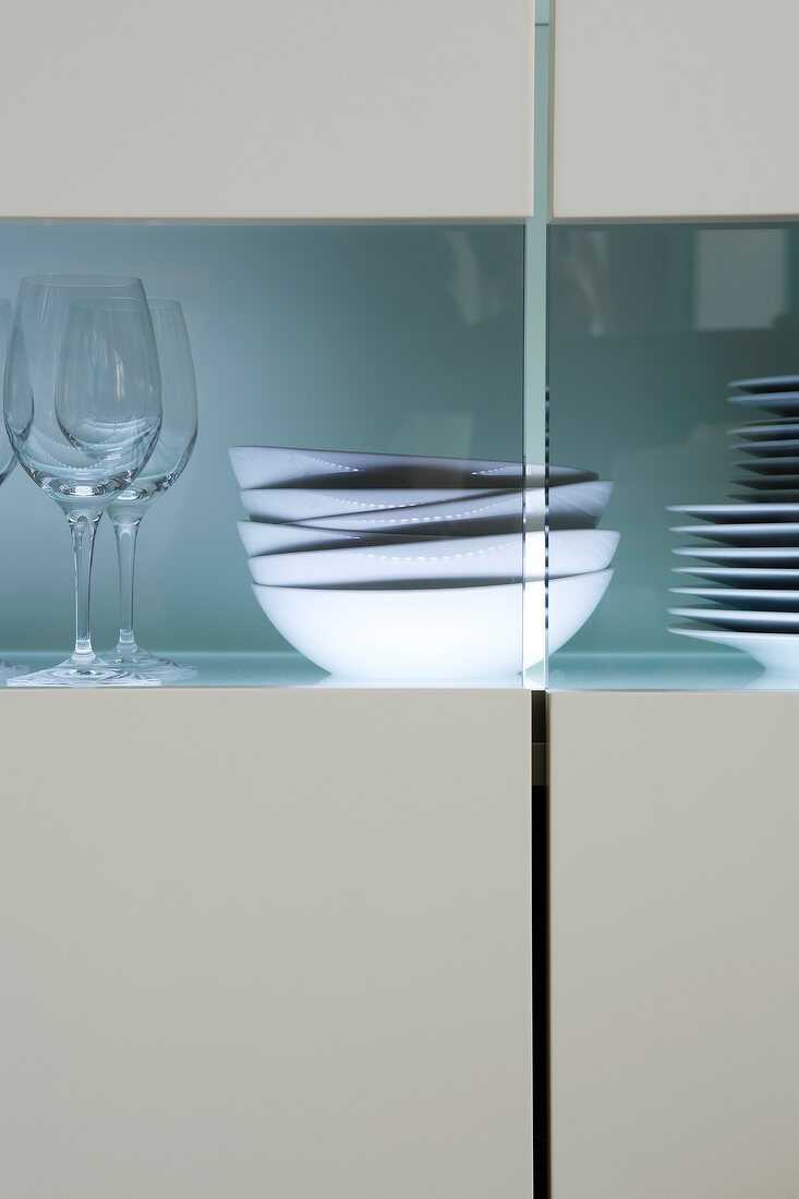 Close-up of illuminated sideboard with white bowls and wine glasses