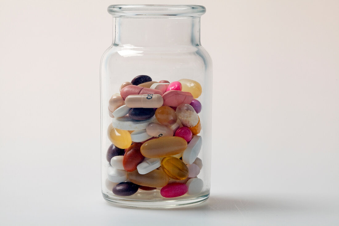 Different pills, tablets, dragees and capsules in glass bottle against white background