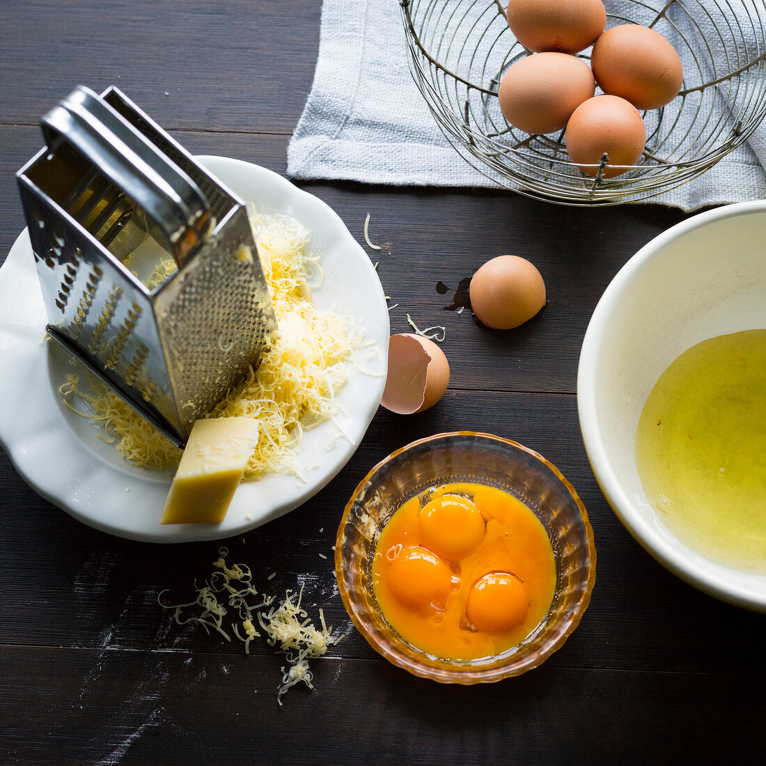 Grated cheese, separate eggs, grater on plate over wooden surface
