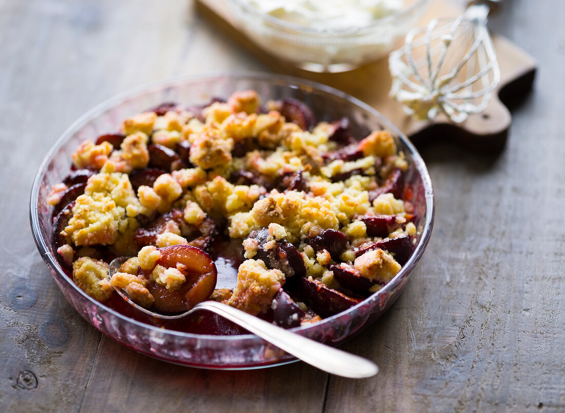 Sliced plums with crumbles and spoon in glass plate