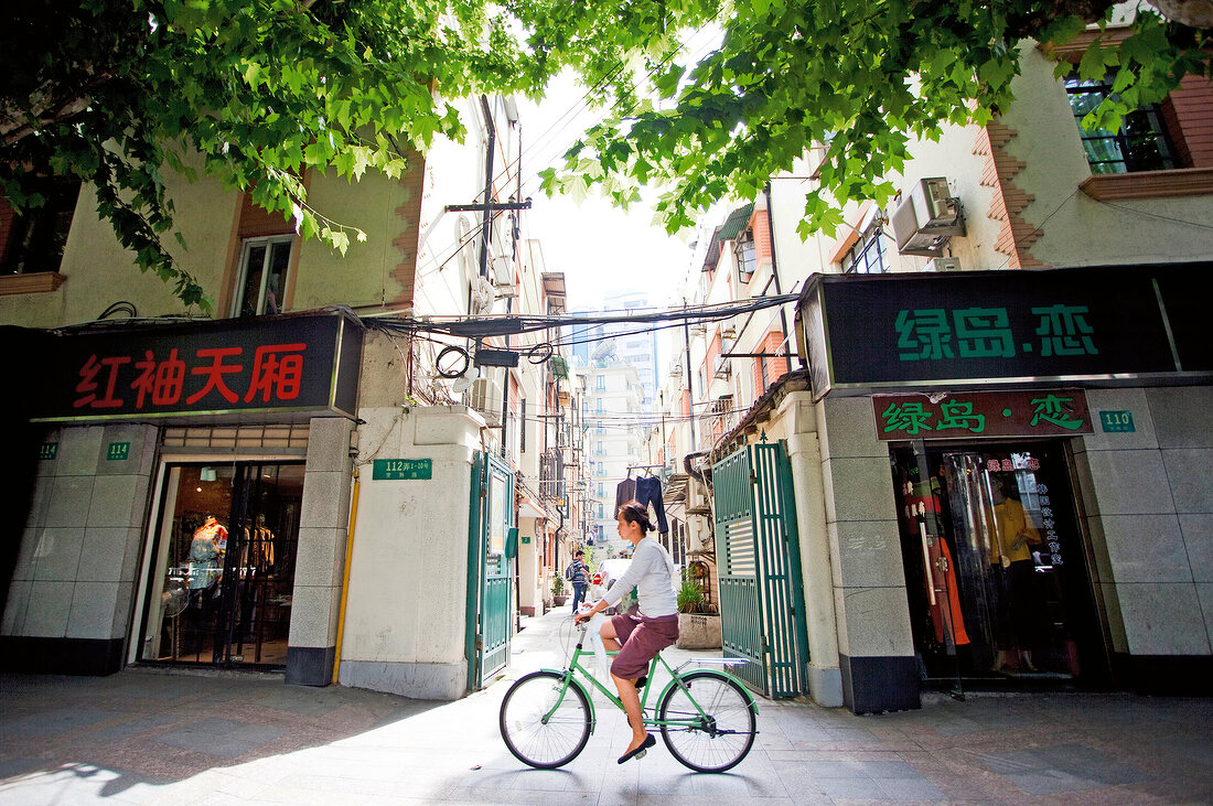 Woman on bicycle against shops at French Concession district, Shanghai, China