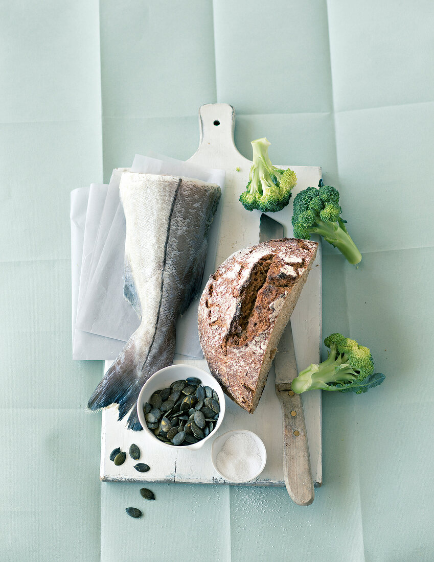 Fish with rye bread, broccoli, pumpkin seeds and salt on chopping board