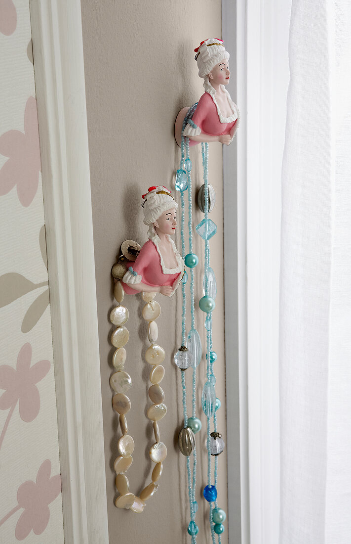 Close-up of necklaces hanging on half woman figurines on wall